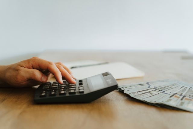 a hand calculating finances with a calculator next to stacks of US dollar bills